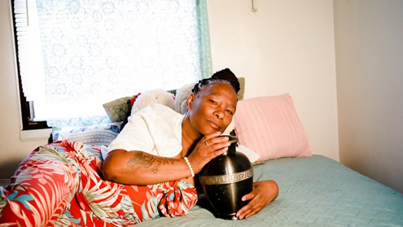 Photo of a Black woman lying on a bed holding an urn