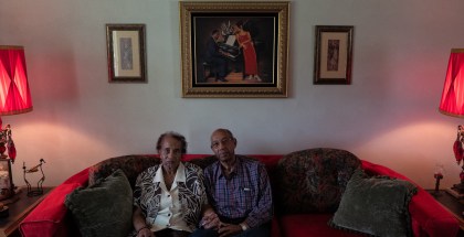 Two people hold hands while sitting close to each other on a red couch