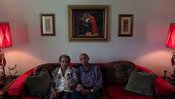 Two people hold hands while sitting close to each other on a red couch