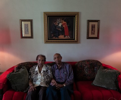 Two people hold hands while sitting close to each other on a red couch